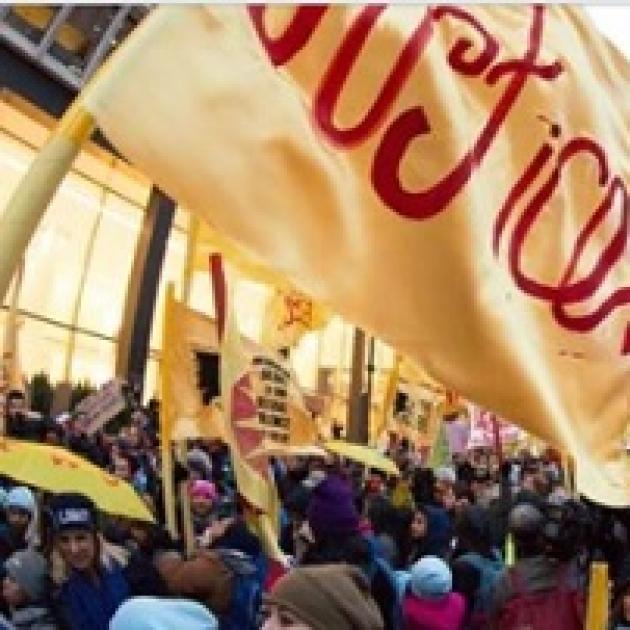 Yellow flag that says Justice in red and lots of people protesting outside