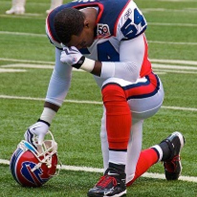 Football player wearing red white and blue football uniform kneeling on field