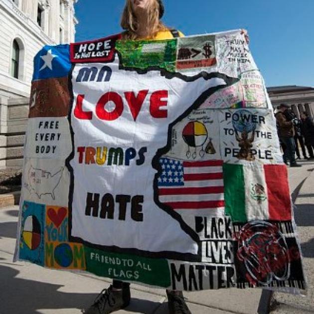 A woman protests Donald Trump with a "Love Trumps Hate" banner/blanket