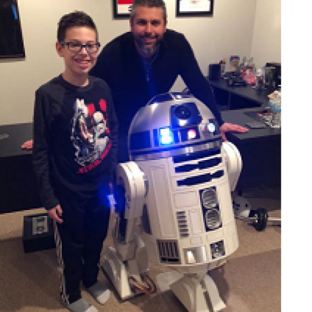 Man and young boy posing next to a robot that has a round top and white round body