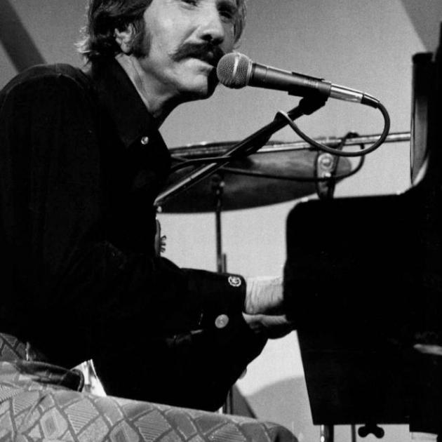 Black and white photo of guy with big mustache sitting at piano singing