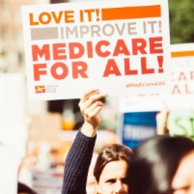Woman holding up a sign saying Medicare For All! Love it! Improve it!