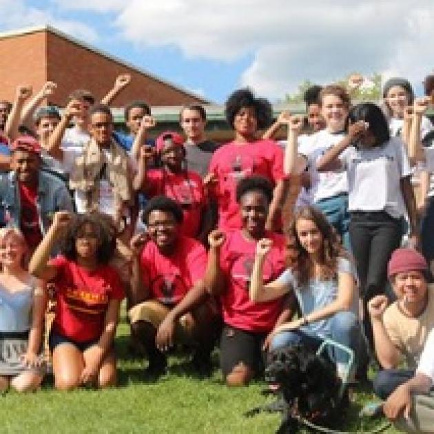 Young people posing outside wearing mostly red shirts with their fists in the air