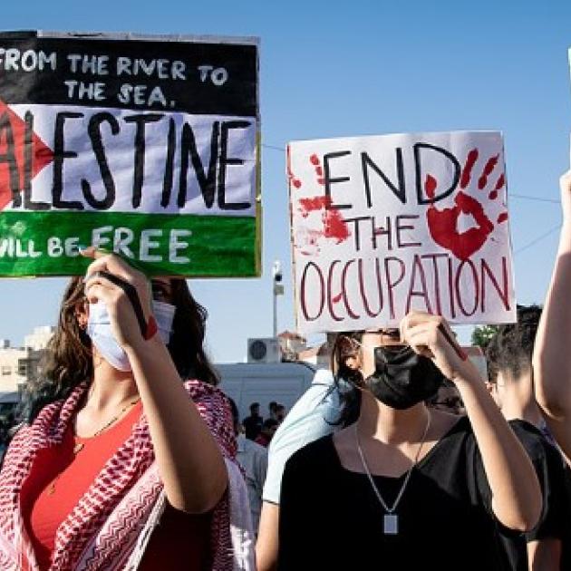 From left to right, protest signs read: "From the river to the sea Palestine will be free", "End the occupation", "End apartheid."