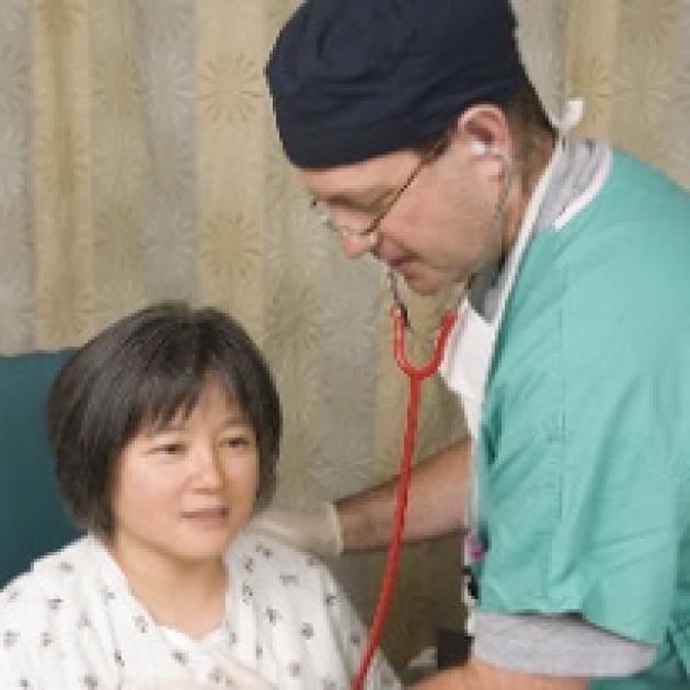 Doctor with scrubs on using stethoscope on a middle aged Asian woman