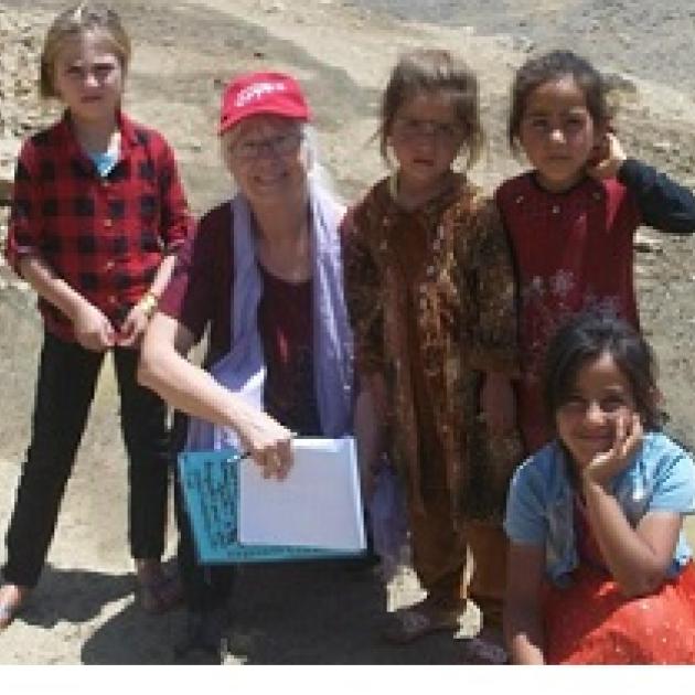 Older gray haired white woman posing outside with four dark skinned young girls