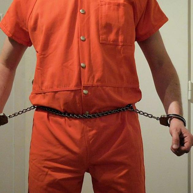 Guy in orange jumpsuit and chain around his belly attached to his wrists