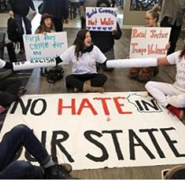 People sitting in a circle on the ground with signs, one in the middle says No hate in our state