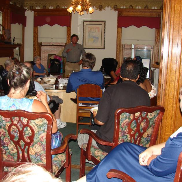 A fancy looking room with people sitting around a table listening to a speaker