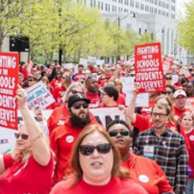 Huge outdoor march with everyone wearing red T-shirts and holding signs that say Fighting for Schools