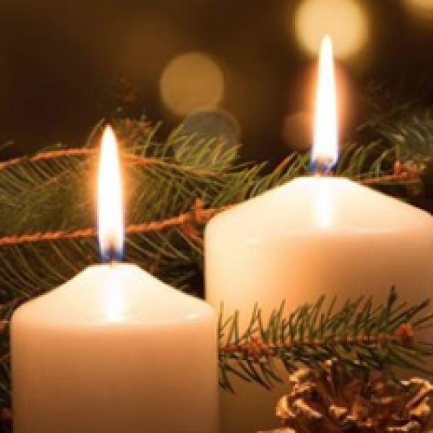 Two candles with close up on flames and pine branches in background