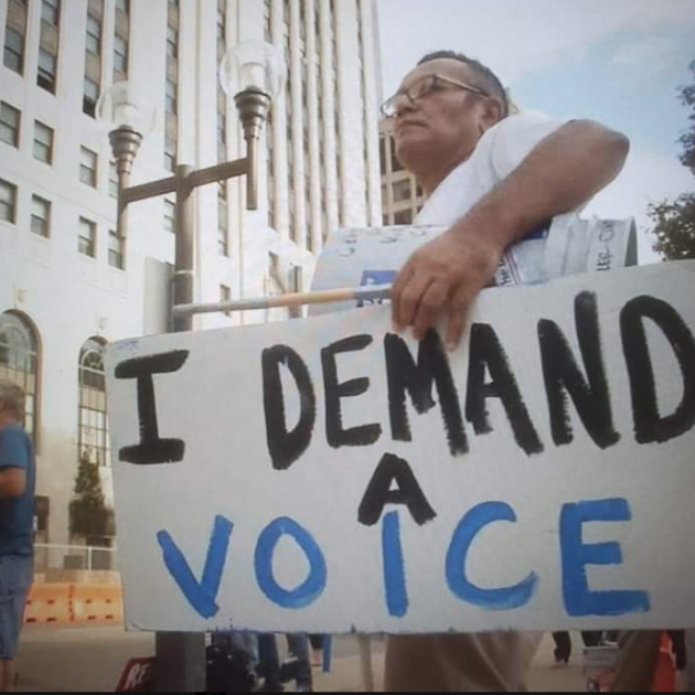 Man holding sign saying I Demand A Voice