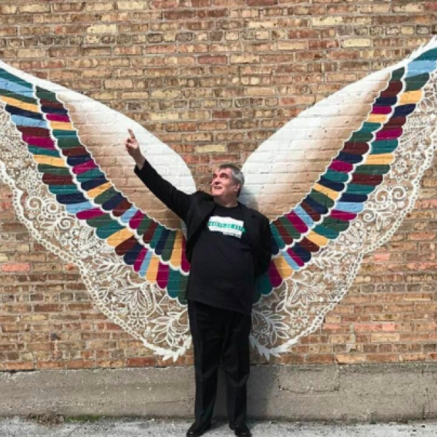 Man standing in front of an art piece of two big wings against a wall