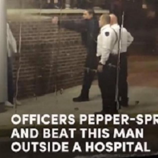 Photo of three white policemen outside one spraying pepper spray at a black man