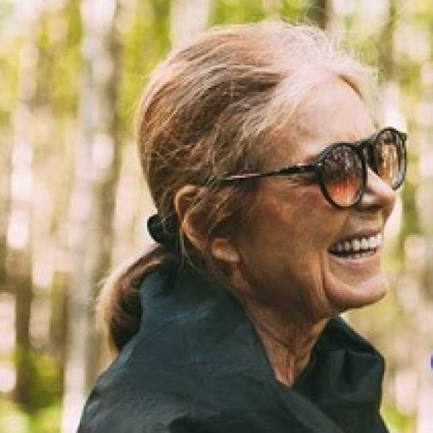 Older woman with big sunglasses facing right in a ponytail, smiling