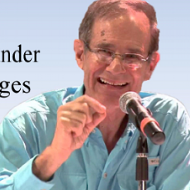 Older balding white man smiling and talking into a mic making a gesture with his hand