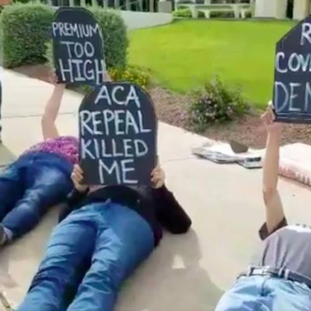 People laying outside on the ground holding tombstone signs that say ACA Repeal killed me
