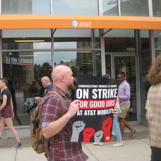Guy in a strike protest holding a sign that says On Strike