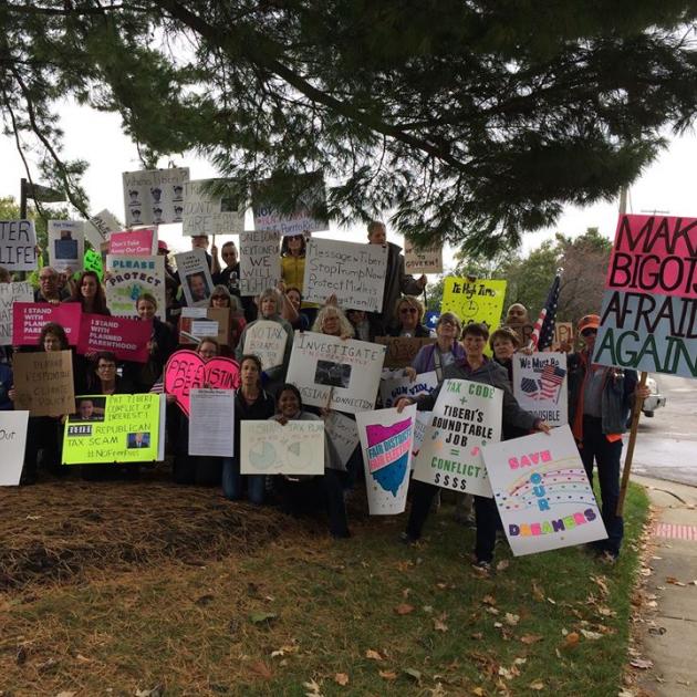 A bunch of people holding signs and facing the camera posing under a tree