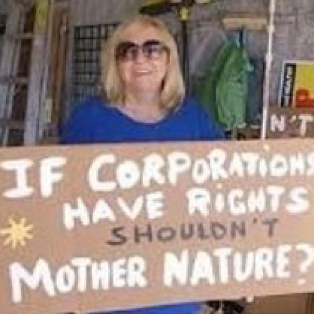 Blonde white woman with sunglasses holding a sign and smiling sign says If Corporations have rights shouldn't mother nature?