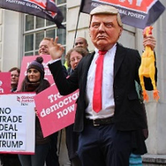 Man wearing Trump mask at demonstration with people holding signs saying No Trade Deal with Trump