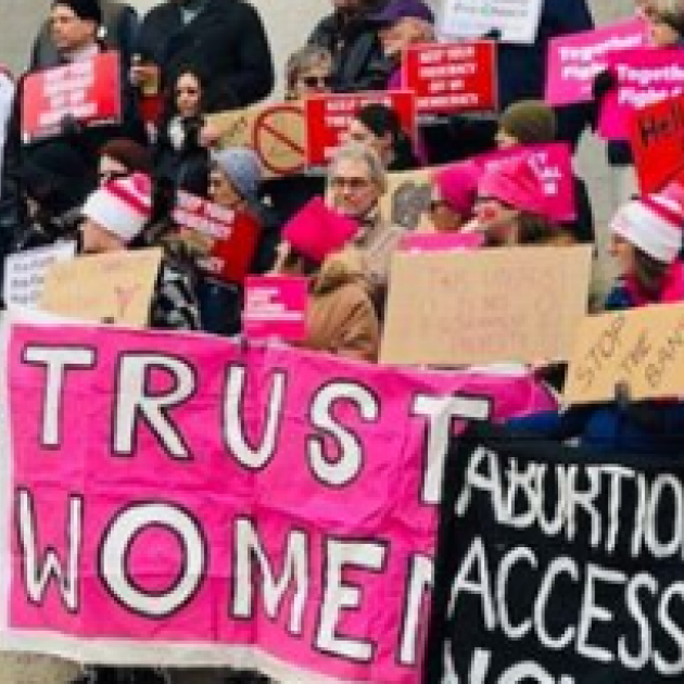 People at a rally holding signs saying Abortion Access and Trust Women