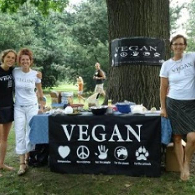 Three happy people by a table outside that says VEGAN on a sign
