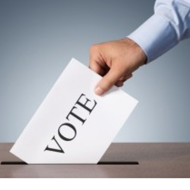 Man's hand putting a paper with the word VOTE on it into a slot in a box