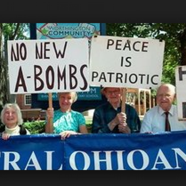 People marching outside with trees in background carrying signs, No New A-Bombs, Peace is Patriotic