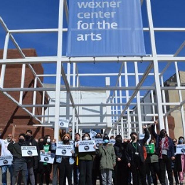 Workers holding signs under the Wexner Center for the Arts sign on building