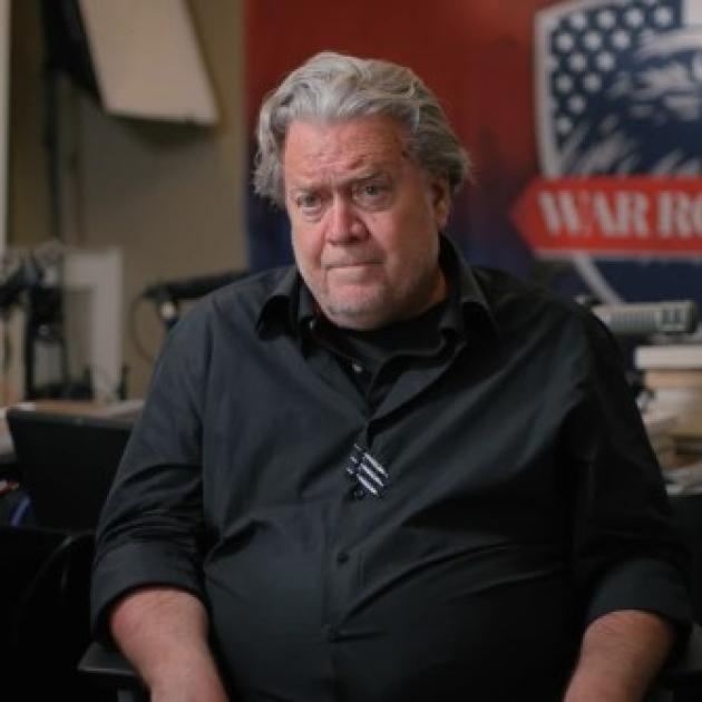 Gray haired white man by a sign reading War Room