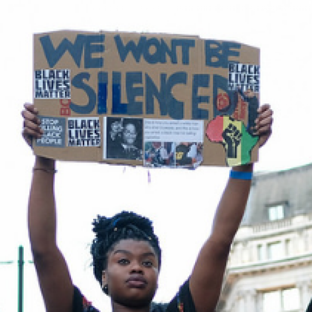 Black woman holding up a sign that says we will not be silenced