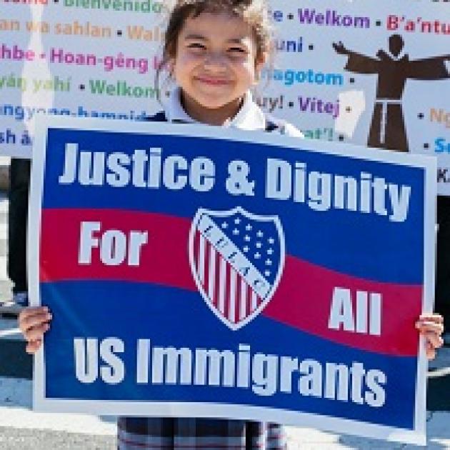 Very young Latino-looking girl holding a red white and blue sign that says Justice & Dignity for all US immigrants