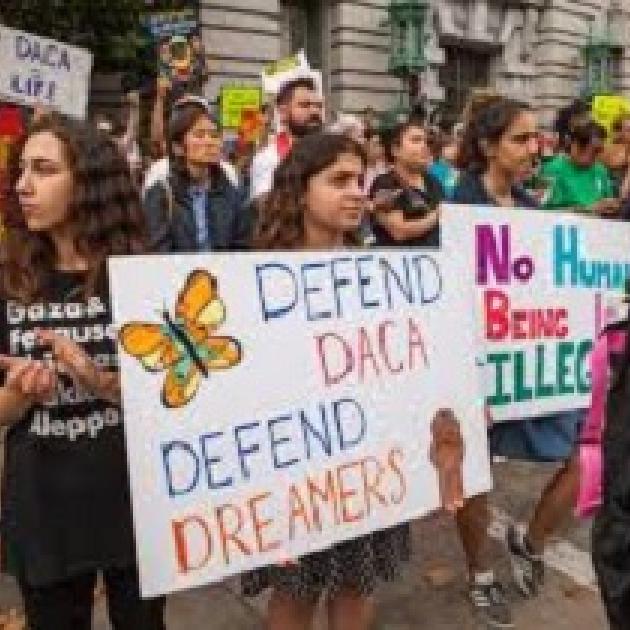 Young people holding signs outside a building that say Defend DACA Defend Dreamers