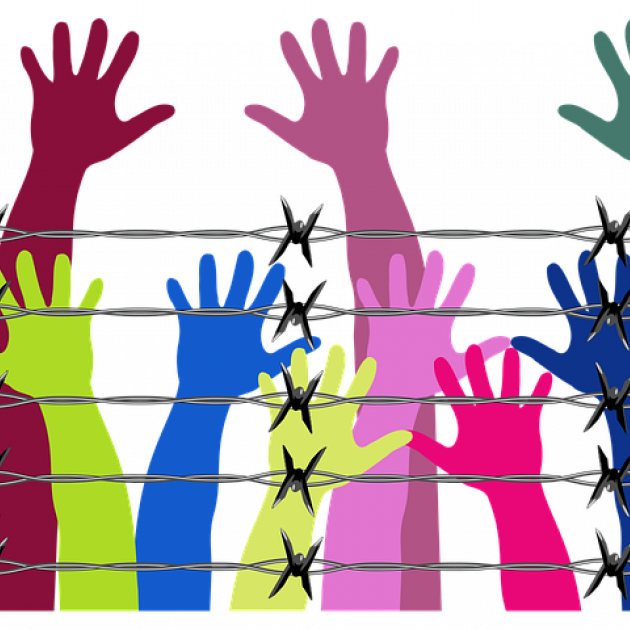 Different color arms and hands reaching up behind a barbed wire fence