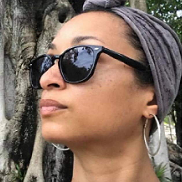 Young black woman with a scarf on her head and sunglasses looking left in front of a tree