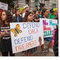 Lots of young kids holding signs outside at a demonstration that say Defend DACA Defend Dreamers and No Human Being is Illegal