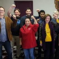 Several people smiling and standing in rows facing the camera with their fists in the air