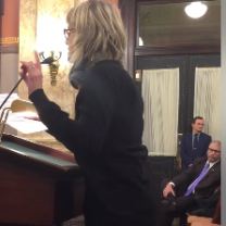 White woman with short blonde hair taking animatedly at a podium