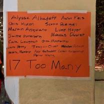 A sign on orange paper taped to a brown wall listing all the names of people killed in the recent Parkland Fla school shooting and the words 17 too many at the bottom 