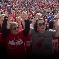 Lots of people in the background and in the foreground two heavyset middle aged ladies holding hands with arms above their heads in victory pose