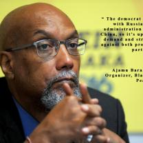 Bald black man with hands folded in front of chin, wearing glasses and with a gray goatee against yellow background and some words