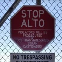 Stop sign in Spanish on a wire fence and sign that says No Trespassing