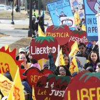 People holding bright red signs shaped like tomatoes that say Justica and Libertad