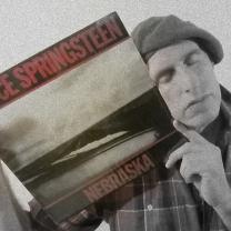 Guy wearing a beret with his eyes closed holding an album cover of Springsteen's Nebraska up to his face