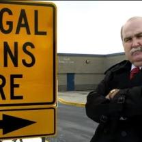 SIgn saying illegal aliens here and a stern bald older man with arms crossed and 