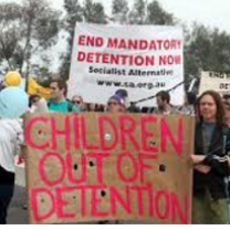 People outside at a rally holding signs saying Children out of detention and End Mandatory Detention Now