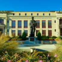 Big white government building with tall gray statue out front and some greenery in the foreground