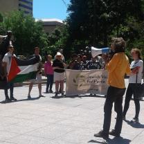 Man speaking into bullhorn and crowd with Jewish Voices for Peace sign