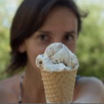 Young white girl with brown hair holding an ice cream cone in front of her face